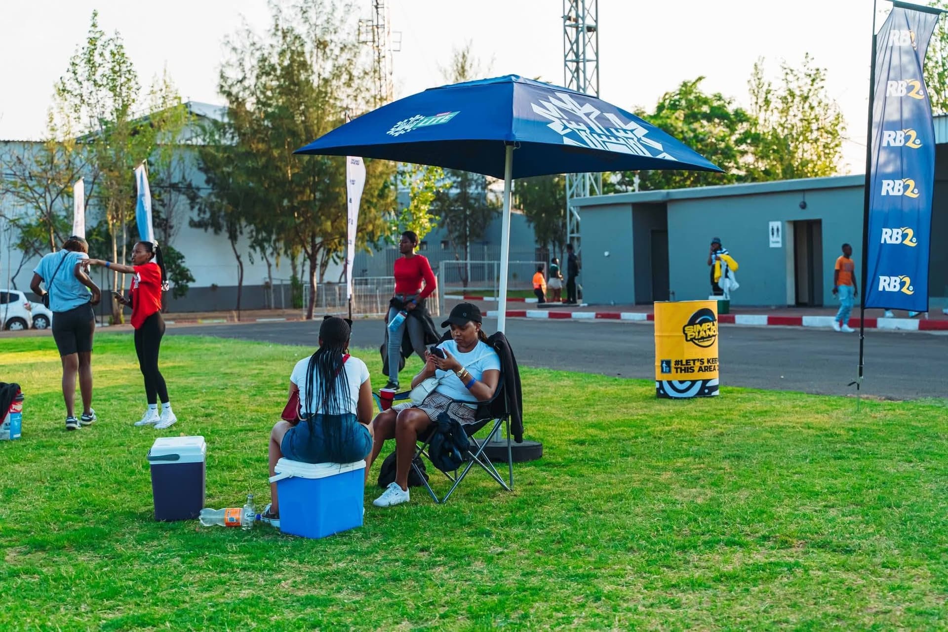 Attendees seated under a branded umbrella on the lawn at a Simply Piano activation